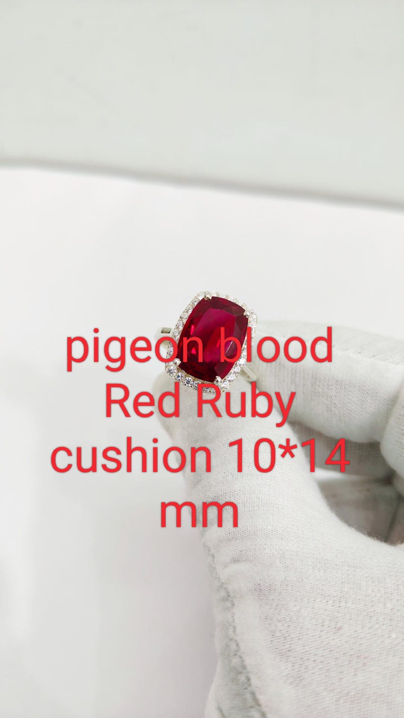 Puede incluir: Anillo de plata con un rub&iacute; rojo de talla coj&iacute;n, rodeado de peque&ntilde;as piedras transparentes. El texto en la imagen dice: "pigeon blood Red Ruby cushion 10*14 mm". El rub&iacute; mide 10 mm x 14 mm.
