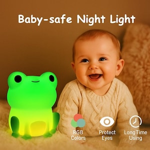 Puede incluir: Una luz de noche verde con forma de rana con el texto "Baby-safe Night Light". La luz tiene colores RGB, protege los ojos y ofrece un uso prolongado. Un bebé sonriente está en el fondo.