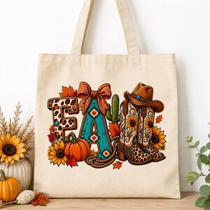 Puede incluir: Una bolsa de tela beige con un estampado gráfico colorido de la palabra FALL. El diseño incluye una letra F con estampado de leopardo, una letra A turquesa con un lazo, una calabaza, girasoles, un cactus y un par de botas vaqueras marrones.