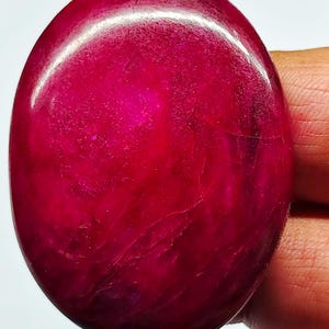 Peut inclure: Une pierre précieuse polie de forme ovale avec une couleur rouge magenta profonde et saturée. La surface de la pierre présente une finition lisse et réfléchissante avec des inclusions naturelles internes visibles et des variations subtiles.