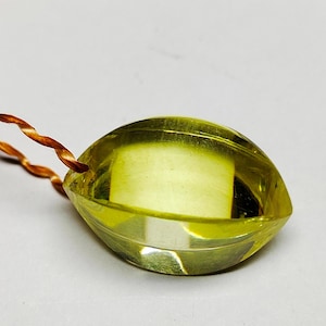 May include: A yellow-green gemstone pendant with a faceted teardrop shape. It is suspended by a twisted, copper-coloured cord. The gemstone has a clear, polished appearance.