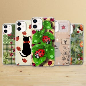 Puede incluir: Cinco fundas para teléfono con varios diseños: mariquitas, un gato negro con pajarita roja y estampados florales. Se muestran sobre una superficie de madera.