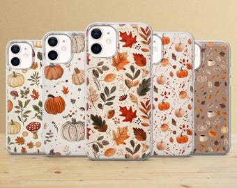 Puede incluir: Cinco fundas transparentes para teléfono con diseños otoñales. Las fundas presentan ilustraciones de calabazas, hojas y setas en tonos naranja, marrón y crema. Las fundas están dispuestas sobre una superficie de madera.