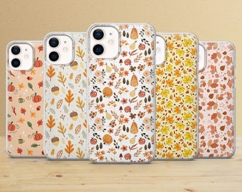 Puede incluir: Cinco fundas para teléfono con diseños otoñales. Las fundas presentan diseños de calabazas, hojas, bellotas y flores en tonos naranja, amarillo y marrón. Las fundas se muestran sobre una superficie de madera.