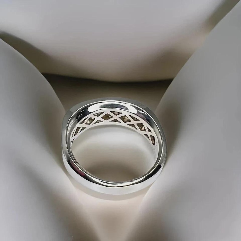 Pu&ograve; includere: Un anello d'argento con un design geometrico. L'anello ha una fascia larga con una serie di piccole pietre quadrate disposte a croce. L'anello &egrave; mostrato su uno sfondo bianco.