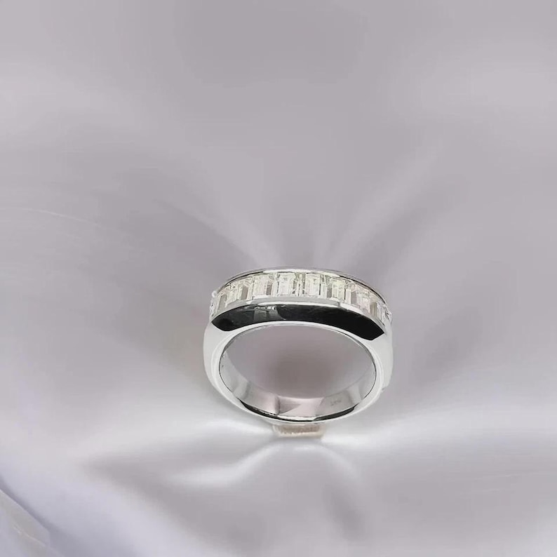 Pu&ograve; includere: Un anello d'argento con una fascia di pietre rettangolari e trasparenti. L'anello ha una fascia spessa con un accento nero. L'anello &egrave; esposto su una superficie bianca strutturata.