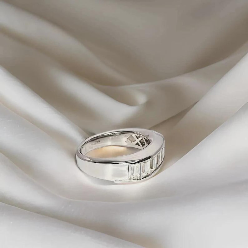 Pu&ograve; includere: Un anello d'argento con una fila di pietre preziose rettangolari e trasparenti. L'anello &egrave; posto su uno sfondo bianco e setoso. Il design dell'anello &egrave; moderno e minimalista, adatto per l'uso quotidiano o per occasioni speciali.