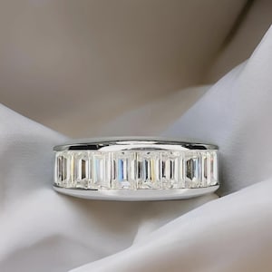Pu&ograve; includere: Un anello d'argento con una fascia di pietre preziose rettangolari e trasparenti. L'anello &egrave; posto su un tessuto bianco drappeggiato, creando un contrasto che ne esalta la lucentezza e il design. Le pietre sono uniformemente distanziate.