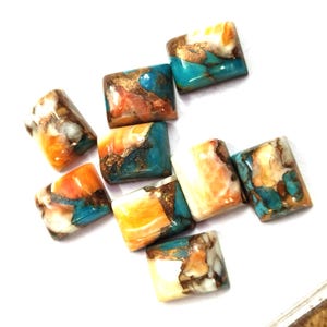 Puede incluir: Un conjunto de ocho cabujones rectangulares con un patrón jaspeado en tonos turquesa vibrante, naranja brillante y blanco crema, con vetas de color cobre metálico en todas las superficies de piedra pulida.