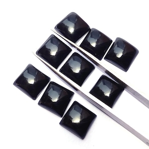 May include: Eight polished black square cabochons arranged in two rows, held by a pair of silver-toned metal tweezers. Each cabochon features a smooth, domed surface with a reflective finish, showcasing a uniform dark colour and sharp, clean edges.