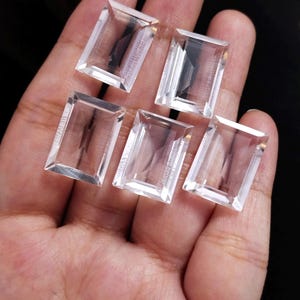 May include: Five clear, rectangular, faceted gemstones arranged in a cluster. Each stone features a transparent, colourless appearance with sharp, geometric edges and a polished surface that reflects light, showcasing a classic step-cut design.