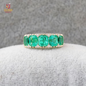 May include: A gold band ring featuring five cushion-cut green emerald gemstones arranged in a row, accented with small round white diamonds set between each emerald. The ring has a polished gold metal finish and a classic, symmetrical design.