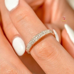 May include: A rose gold band ring featuring three rows of small, clear, round-cut pavé-set stones that cover the outer surface of the metal. The ring has a polished finish and a uniform width, displaying a logo with the text EJ Jewels.