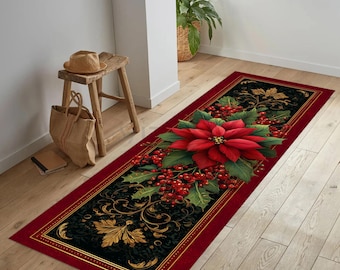 Op de afbeelding: Een rechthoekige rode loper met een zwart middenstuk met een grote rode poinsettia bloem, groene bladeren en rode bessen. Gouden filigraan en een gouden rand omlijsten het ontwerp. De loper ligt op een houten vloer.