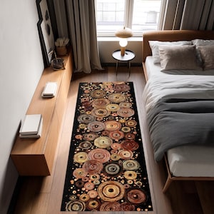 May include: A rectangular rug with a black background and a pattern of overlapping circles in shades of brown, gold, and copper. The circles vary in size and density, creating a textured appearance. The rug is placed in a bedroom setting.