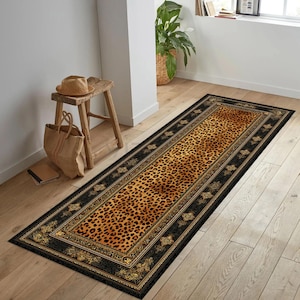 May include: A rectangular runner rug with a leopard print center and a black border with gold accents. The rug is placed on a wooden floor, adding a touch of luxury to the space.