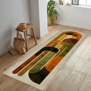 Op de afbeelding: Een rechthoekig tapijt met een abstract ontwerp in tinten oranje, groen, bruin en geel. Het tapijt heeft gebogen en rechte lijnen, waardoor een geometrisch patroon ontstaat. Het tapijt ligt op een houten vloer.