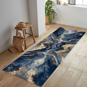 Può includere: Un tappeto rettangolare con un design marmorizzato nei toni blu navy, grigio e oro. Il tappeto presenta un motivo astratto e fluido con accenti dorati, creando un aspetto lussuoso e artistico. Il tappeto è posato su un pavimento in legno.