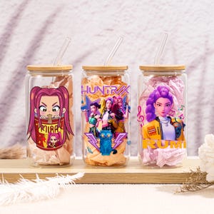 Puede incluir: Tres frascos de vidrio para beber con tapas de bambú y pajitas de vidrio. Cada frasco presenta un gráfico colorido de un personaje de dibujos animados o un grupo de personajes. Los frascos están llenos de papel decorativo.