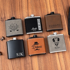 May include: Six personalised hip flasks in various colours, including grey, black, and brown, with silver tops. The flasks feature engraved names, dates, and designs such as golf clubs, a tuxedo, and a mustache. The flasks are arranged on a wooden surface.