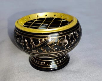 Könnte beinhalten: Ein schwarzer Räuchergefäß mit goldenen Akzenten. Der runde Brenner hat ein florales Muster und eine Gitteroberseite. Der Sockel ist schwarz mit goldenen Verzierungen, das Design ist aufwendig.