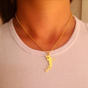 Könnte beinhalten: Eine goldfarbene Halskette mit einem Anhänger in Form eines Handballspielers in Aktion. Der Anhänger hängt an einer zarten Goldkette. Die Halskette wird vor einem weißen Hintergrund gezeigt.