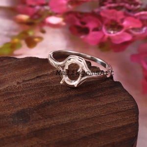 May include: A silver ring setting featuring an oval-shaped prong mount for a gemstone. The metal band has a smooth, polished finish and a split shank design. The text MalikgemsArt is visible across the center of the ring setting.