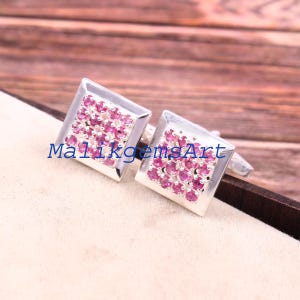 May include: Silver square cufflinks, each set with numerous small, pink gemstones. The cufflinks have a shiny finish and are displayed on a neutral surface. The image includes the text "MalikgemsArt".