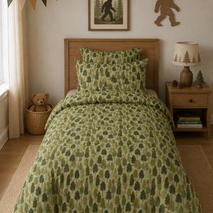 May include: A bed with a green and brown tree pattern duvet cover and pillowcases. The room has a wooden headboard, a framed Bigfoot print, and a Bigfoot cutout. A lamp with a tree design and a teddy bear in a basket are also visible.