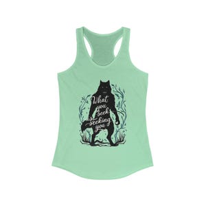 May include: A light green racerback tank top featuring a black silhouette of a werewolf with the text "What you seek is seeking you." The design includes floral and leaf accents around the werewolf.