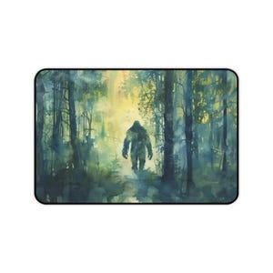 May include: Rectangular mousepad featuring a watercolor painting of a Bigfoot figure walking through a misty forest. The artwork uses shades of green, blue, and yellow, creating a mysterious and atmospheric scene. The mousepad has a black border.
