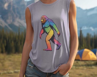 May include: A sleeveless gray tank top featuring a colorful Bigfoot graphic. The Bigfoot is depicted in rainbow hues, walking across the front of the shirt. The background shows a mountain range and camping tents.