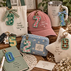 May include: A collection of fabric number keychains featuring various patterns like floral, gingham, and plaid, attached to items including a canvas tote, a pink corduroy cap, a blue corduroy pouch, a white mug, and a star-shaped pillow.