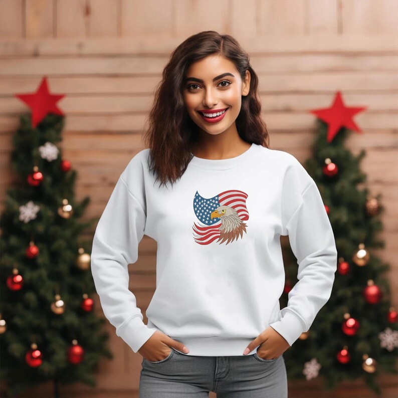 May include: White sweatshirt featuring an embroidered design of an American flag and a bald eagle. The eagle is brown and white, and the flag has red and white stripes with a blue field of stars. The sweatshirt is long-sleeved and has a crew neck.