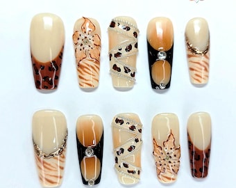May include: A set of ten press-on nails featuring a beige base with various designs including brown leopard spots, tiger stripes, hand-painted flowers, silver chain accents, and clear rhinestones. The logo VEEVEE NAIL ART is visible at the top.