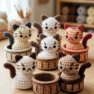 Könnte beinhalten: Eine Sammlung von fünf kleinen gehäkelten Katzenfiguren, die jeweils in einem passenden gehäkelten Korb sitzen. Die Katzen haben verschiedene Farben wie Weiß, Creme und Pfirsich, mit dunkelbraunen oder grauen Ohren und Schwänzen.