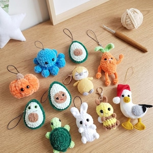 Könnte beinhalten: Eine Sammlung kleiner, handgefertigter Häkel-Plüsch-Schlüsselanhänger mit verschiedenen Figuren, darunter ein blauer Oktopus, ein orangefarbener Kürbis, grüne Avocadohälften, ein gelbes Küken, eine Karotte, eine grüne Schildkröte, ein weißer Hase und eine Möwe.