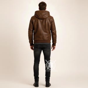 May include: A brown leather jacket with a hood and a ribbed hem. The jacket is worn with dark wash jeans and black boots. The model is facing away from the camera.