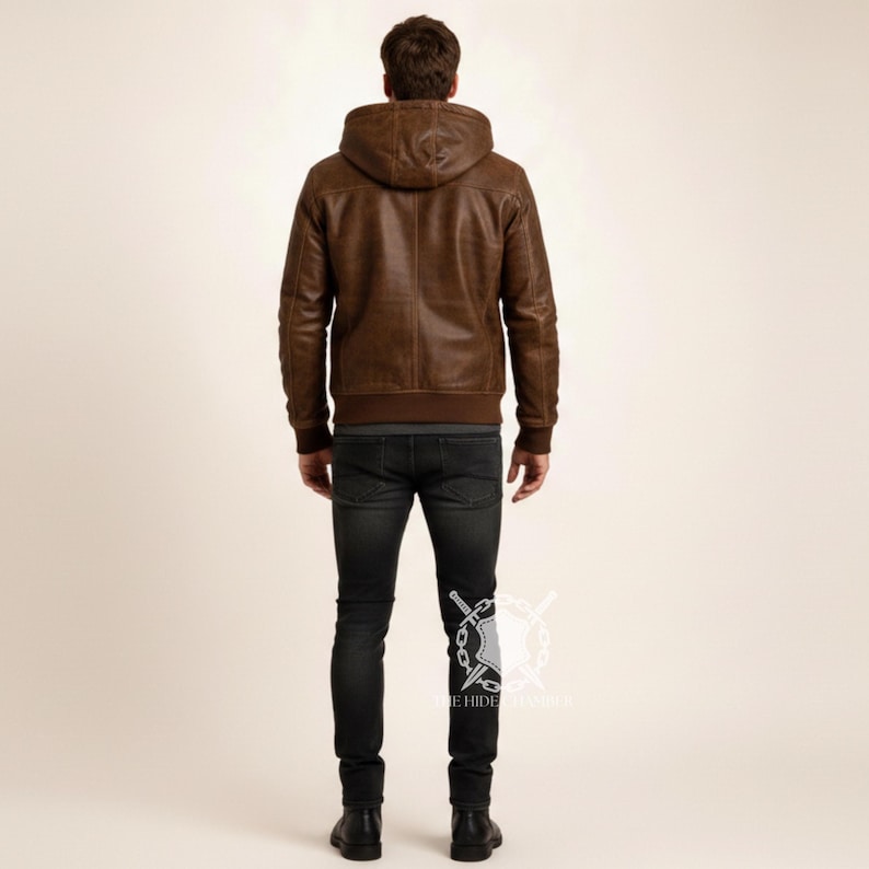 May include: A brown leather jacket with a hood and a ribbed hem. The jacket is worn with dark wash jeans and black boots. The model is facing away from the camera.