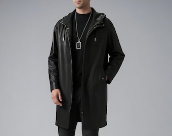 May include: A black leather hooded coat with a longline silhouette. The coat features a front zipper closure, side pockets, and a silver-toned pendant necklace. The model is wearing a black turtleneck and black pants.