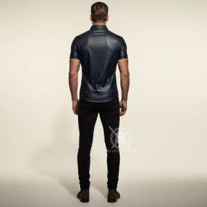 Pu&ograve; includere: Una camicia di pelle blu navy a maniche corte con colletto button-down. La camicia &egrave; abbinata a jeans skinny neri e scarpe marroni. La persona &egrave; vista da dietro.