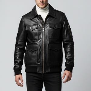 Könnte beinhalten: Schwarze Lederjacke mit Reißverschluss, vier Vordertaschen und einem Kragen. Die Jacke hat einen klassischen Bomberstil mit geripptem Saum und Bündchen. Das Model trägt einen weißen Rollkragenpullover darunter.