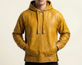 May include: Mustard yellow leather hoodie with a drawstring hood and front pockets. The jacket has a zipper on each side of the waist and silver-colored metal accents on the drawstrings.