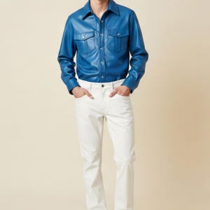 Könnte beinhalten: Eine Person trägt ein leuchtend blaues Lederhemd mit zwei Brusttaschen und eine weiße Hose. Das Hemd hat einen klassischen Kragen und einen Knopfverschluss. Die Hose ist im geraden Stil.