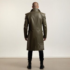 May include: Olive green leather coat with shoulder accents and a long, tailored fit. The coat features a notched collar, long sleeves, and a button-down front. The model is wearing black pants and boots. The coat is approximately 55 inches long.