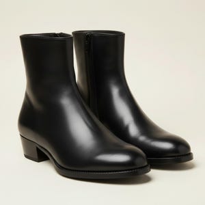 Könnte beinhalten: Ein Paar schwarze Leder-Ankle Boots mit kleinem Absatz. Die Stiefel haben eine glatte, polierte Oberfläche und einen seitlichen Reißverschluss. Das Design ist schlicht und klassisch, passend für verschiedene Outfits.