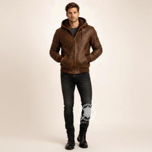 May include: A brown leather hooded jacket with a zipper closure and front pockets. The jacket is worn with black jeans and black boots. The model is standing in front of a neutral background.