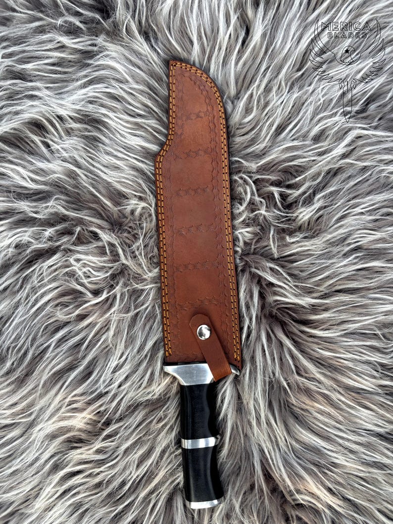 May include: A hunting knife with a brown leather sheath. The sheath is stitched with tan thread and has a silver snap closure. The knife handle is black with silver accents. The blade is partially visible.