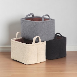 Può includere: Tre cesti portaoggetti rettangolari impilati. I cesti sono realizzati in un tessuto strutturato color crema, grigio e nero. Ogni cesto ha un interno marrone scuro e due manici ad arco.