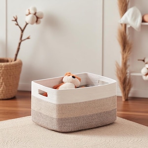 May include: A rectangular storage basket in white, beige, and brown tones. A stuffed fox toy rests inside. The basket has a woven texture and two handles. The basket's dimensions are approximately 30 cm in length, 20 cm in width, and 15 cm in height.